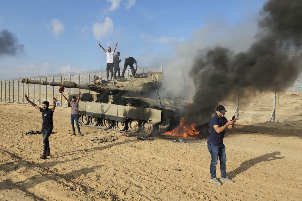 FILE - Palestinians celebrate by a destroyed Israeli tank at the Gaza Strip fence east of Khan Younis Saturday, Oct. 7, 2023.