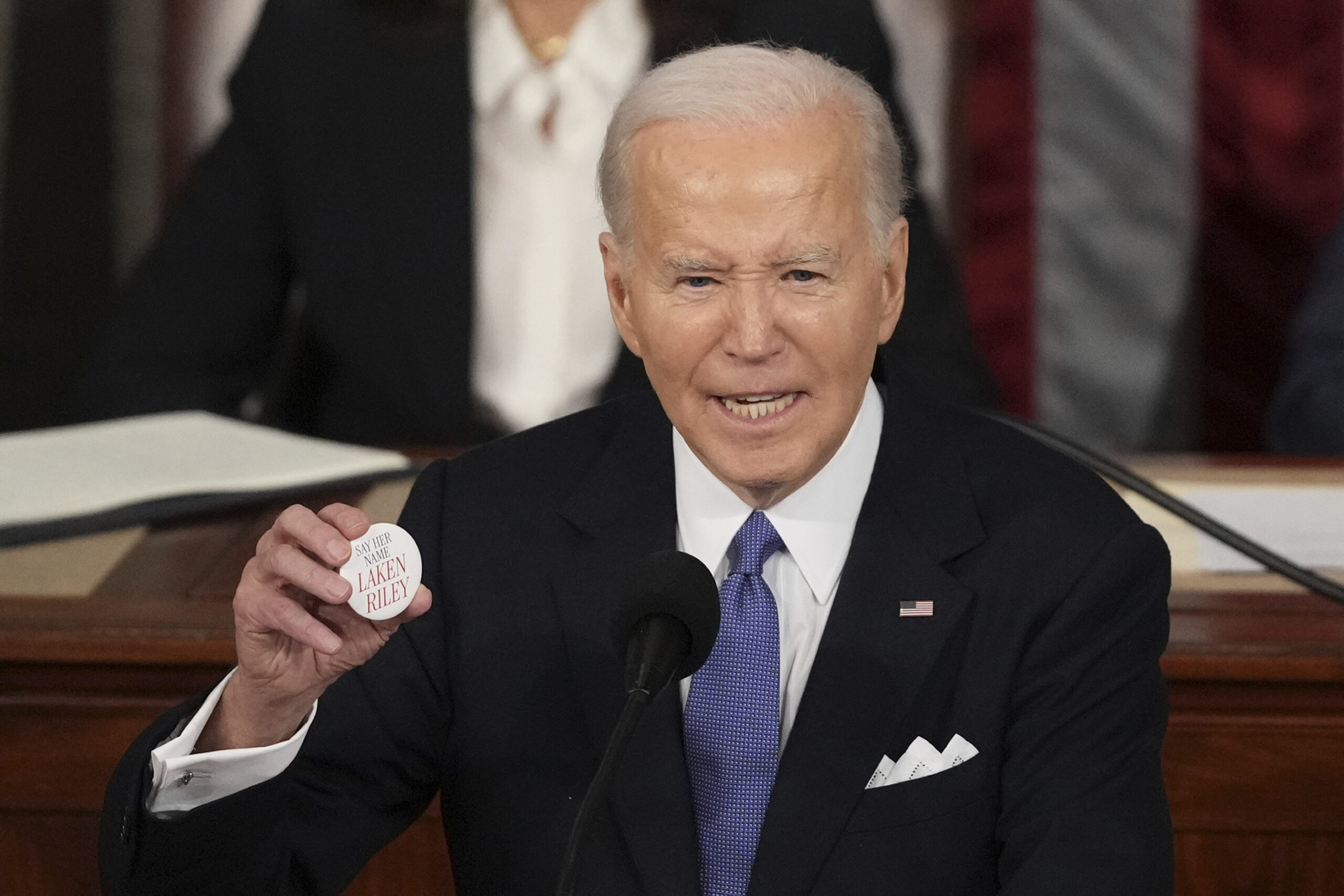 President Joe Biden holds up a Laken Riley button