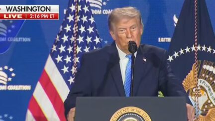 Donald Trump at a microphone with an american flag behind him