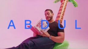 el-sayed with a pink background lounging on an inflatable palm tree and the word abdul in blue letters over laid on the screen