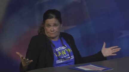 woman in a black blazer and blue t shirt with her arms spread out looking at the audience
